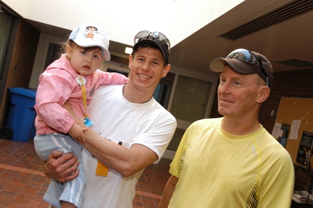 Man smiling while holding a baby girl in his arms and a man standing beside him