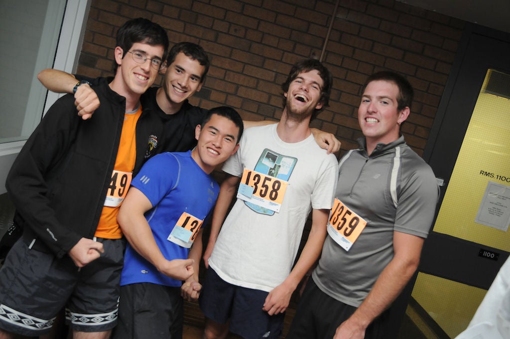Five runners similing towards a camera inside of Applied Health Sciences building after the race