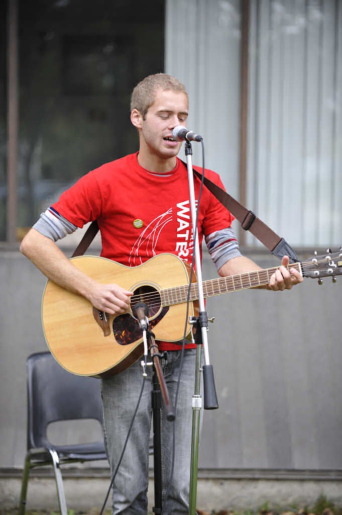 A man with a University of Waterloo shirt performing a song with his guitar