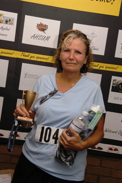 Female holding a trophy and two water bottles in front of the AHS Fun Run and other bulletin board
