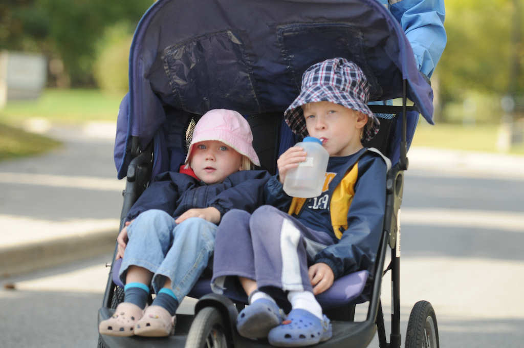Two little kids in one baby stroller while one of them drinking water