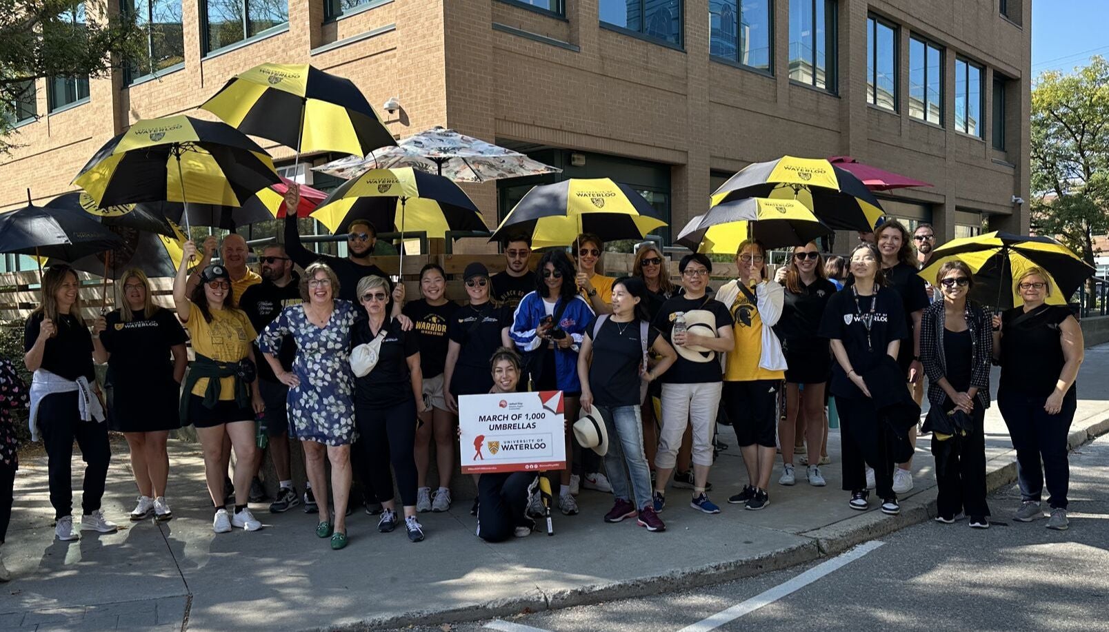 A group of staff, students and faculty from the University of Waterloo stand with black and gold umbrellas for the March of 1000 Umbrellas United Way event.