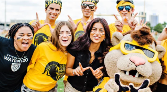 A group of students in Waterloo-branded clothing pose for a photo with the Warriors mascot.
