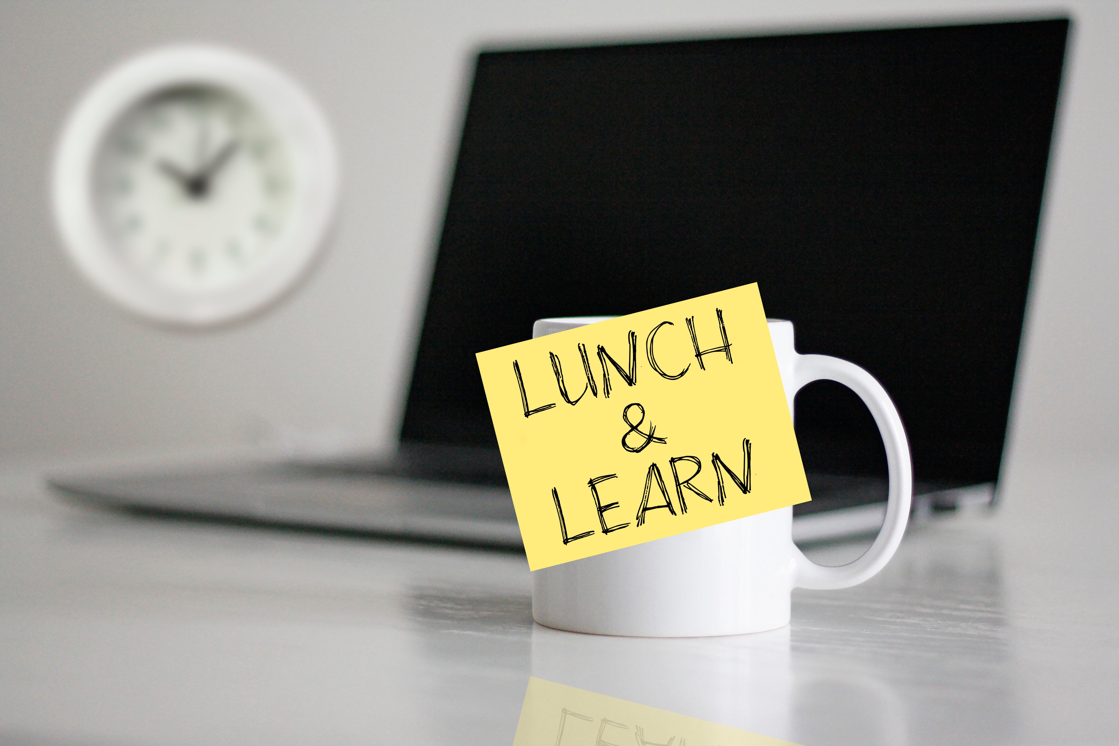 A laptop and mug with a sticky note that reads 'Lunch & Learn'.