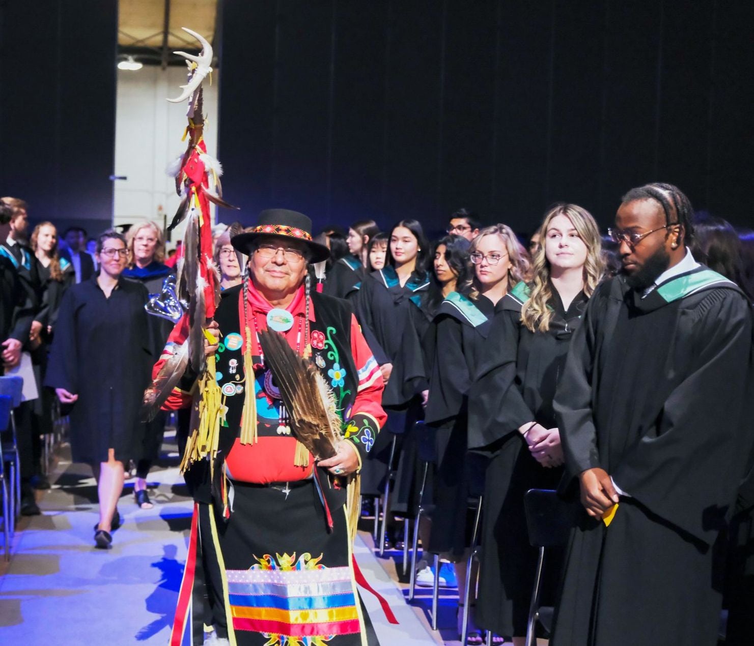 Elder Myeengun Henry walks through a crowd of convocating Health students.