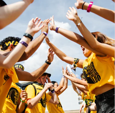 A group of students dressed in Waterloo-branded clothing cheer with their hands in the air.