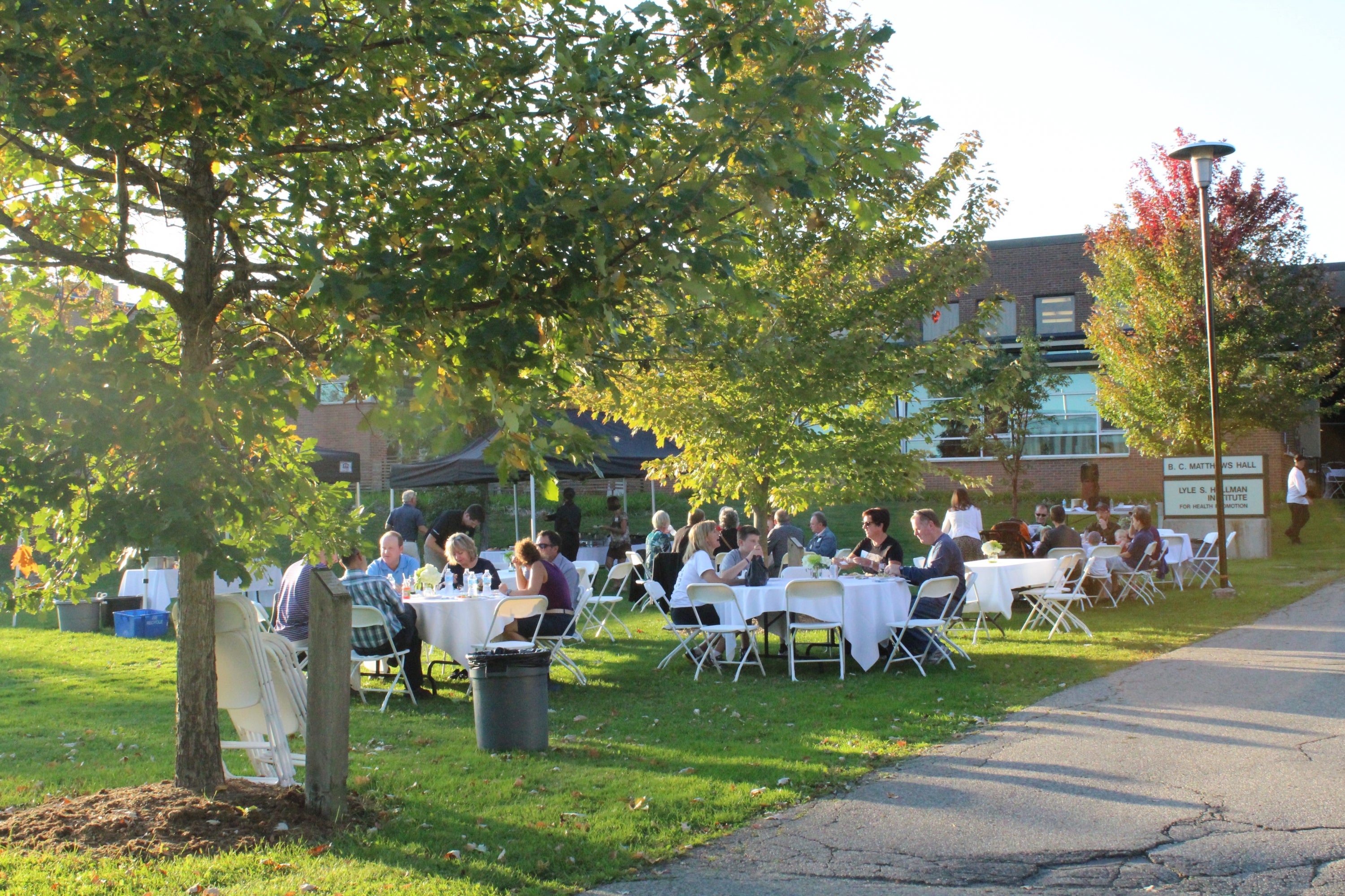 Welcome BBQ with tables of guests on the BMH Green at dusk.