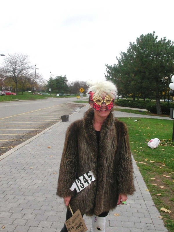 One female paricipant wearing a fur coat and a butterfly mask holding a sign.