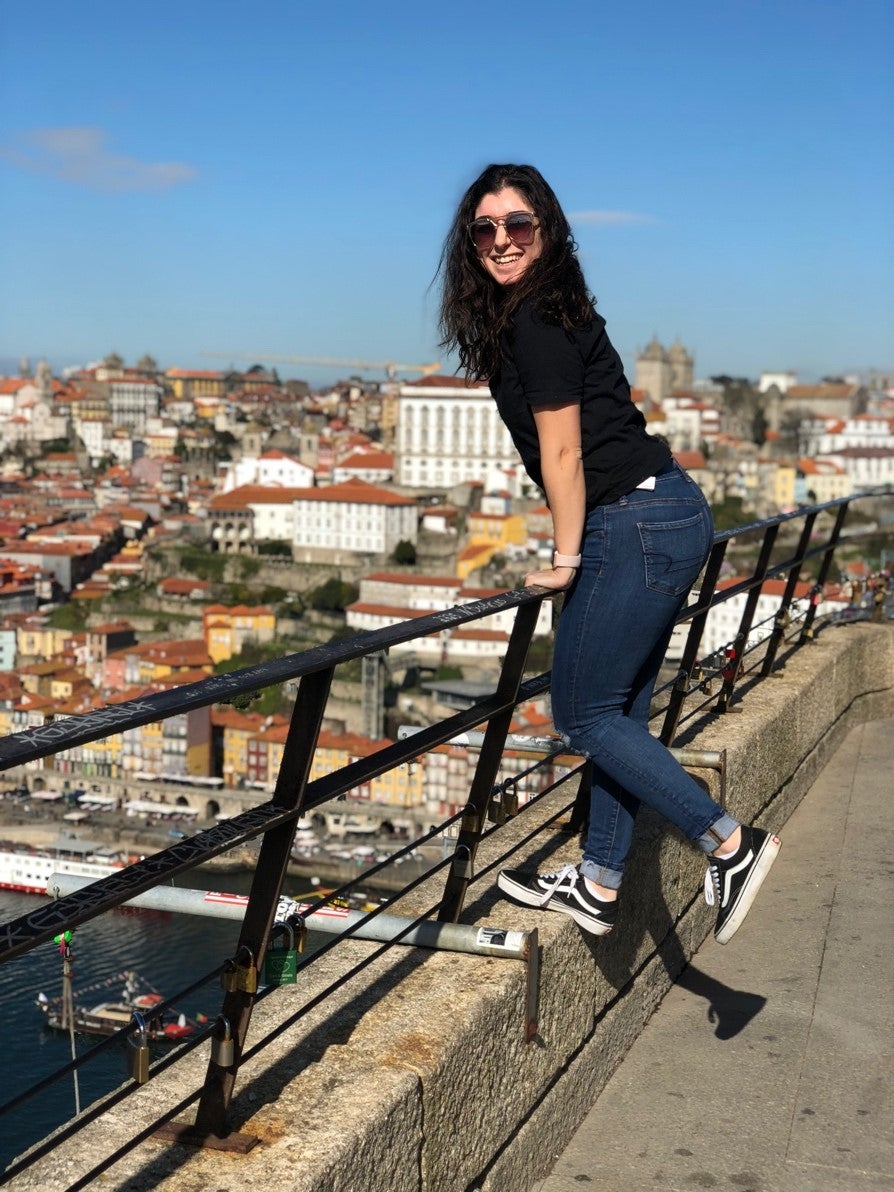 Aysun balancing on the railing of a bridge overlooking a city.