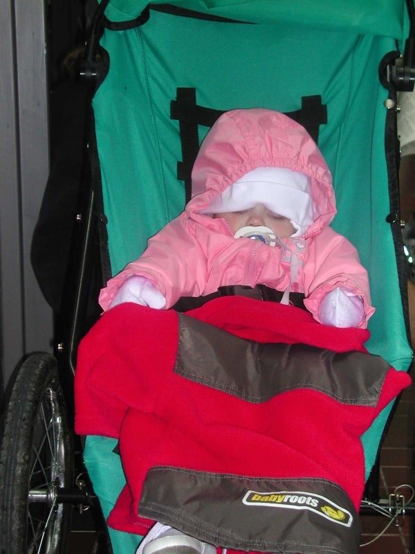 A little baby in a pink jacket sleeping in a baby stroller.