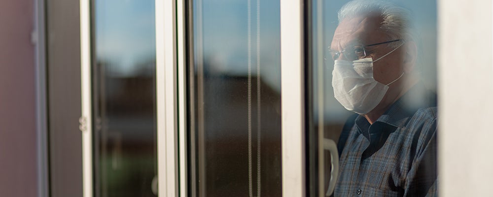 Elderly man with mask looking out of window