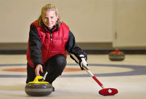Smiling female curler releases rock down ice.