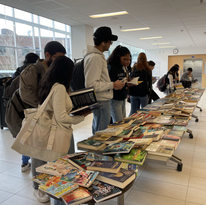 Students browse books that are spread about on a long table.