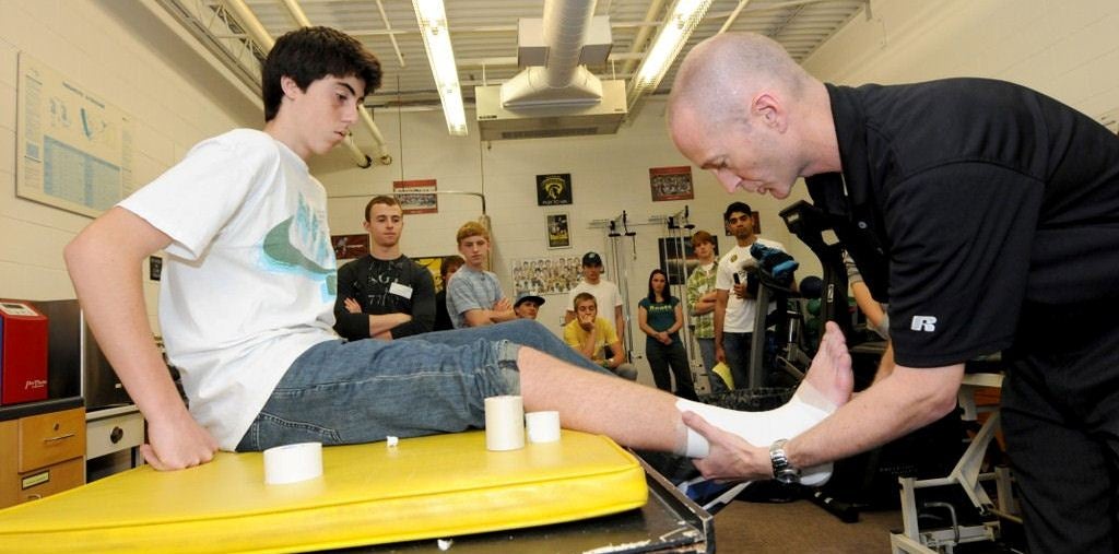 athletic therapist demonstrating how to tape an athlete's ankle