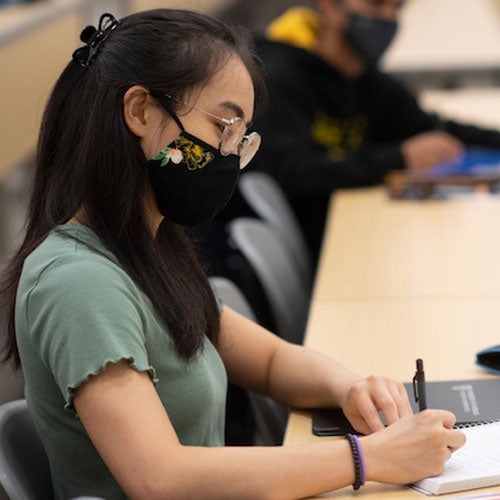 Person sitting at a desk with a mask on writing on paper