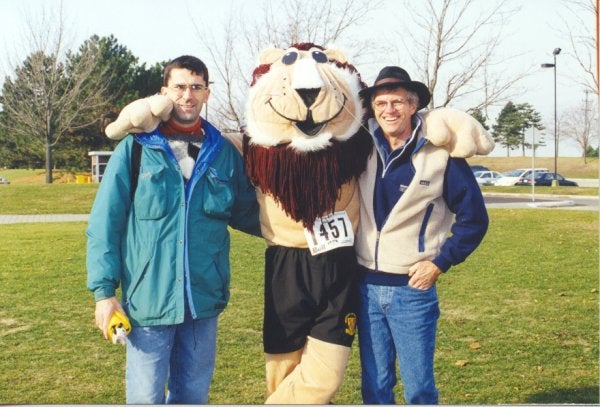 Two men standing with a lion mascot in the middle