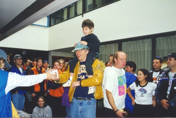 After the race, A boy is sitting on his dad's shoulders while dad is shaking hands with one of the staffs