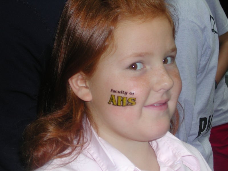 A girl with sticker tatoo written "Faculty of AHS" on her face