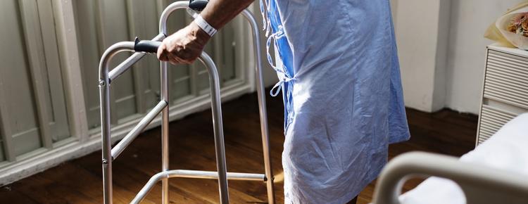 Older adult in a hospital gown using a walker