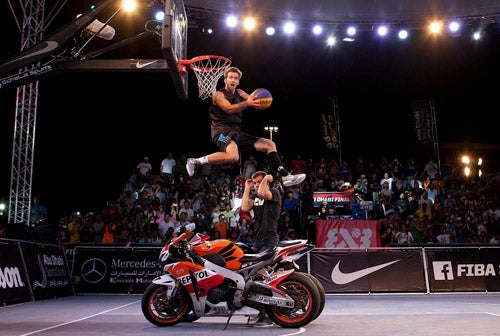 Jordan Kilganon making a dunk shot over man on motorcycle.