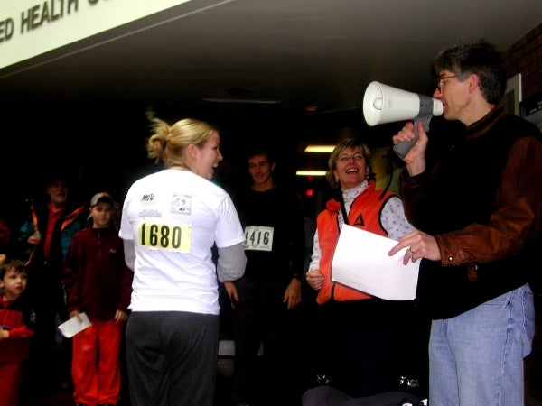 A female runner receiving a prize after the race, one male is talking throught a megaphone