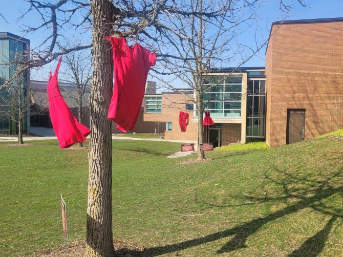 Red dresses blow in the wind, hanging from trees on campus