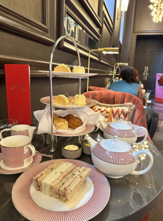 Beatrice enjoying a traditional British afternoon tea with a selection of sandwiches, pastries, and tea