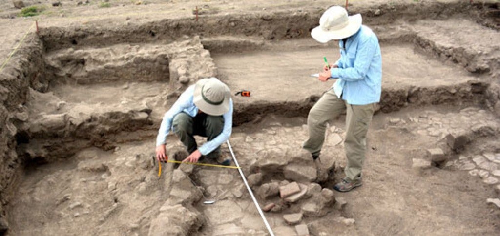 Two archaeologists working in an excavation dig site, measuring artifacts