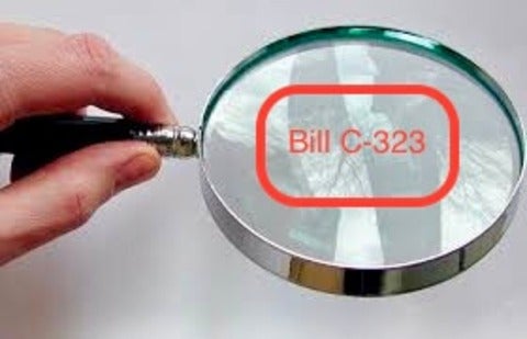 A hand holding a magnifying glass with the words "Bill C-323" in red placed in the center