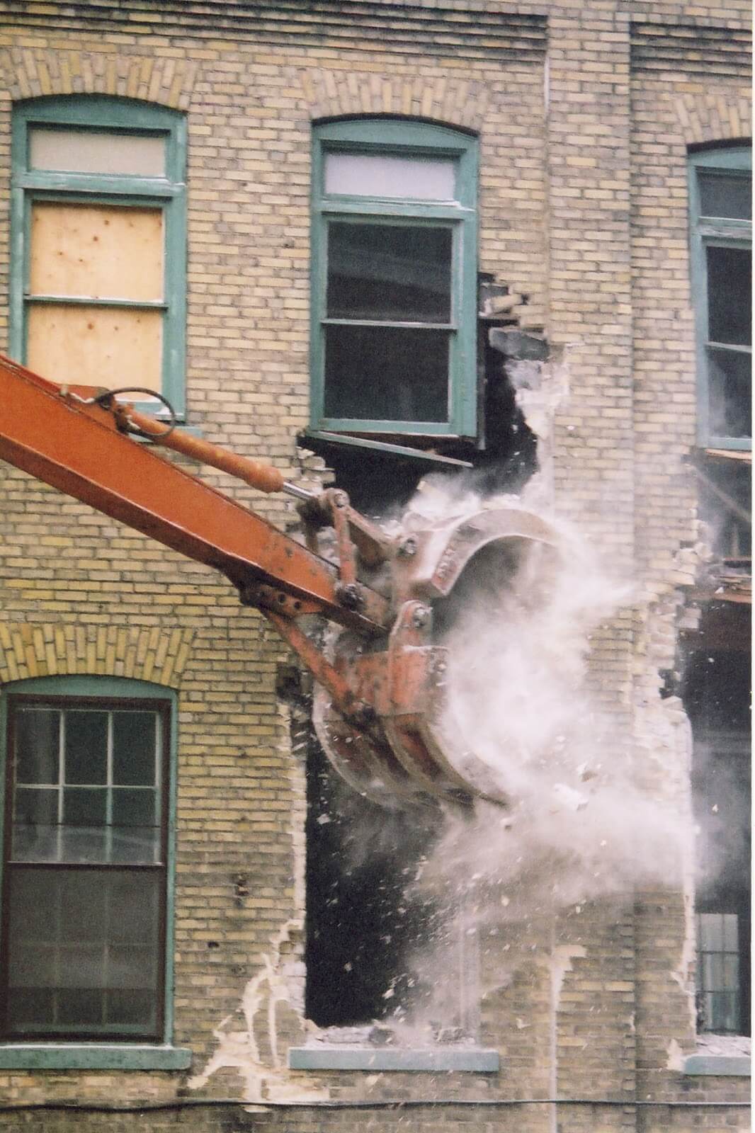 The arm of a bulldozer tearing down a stone building