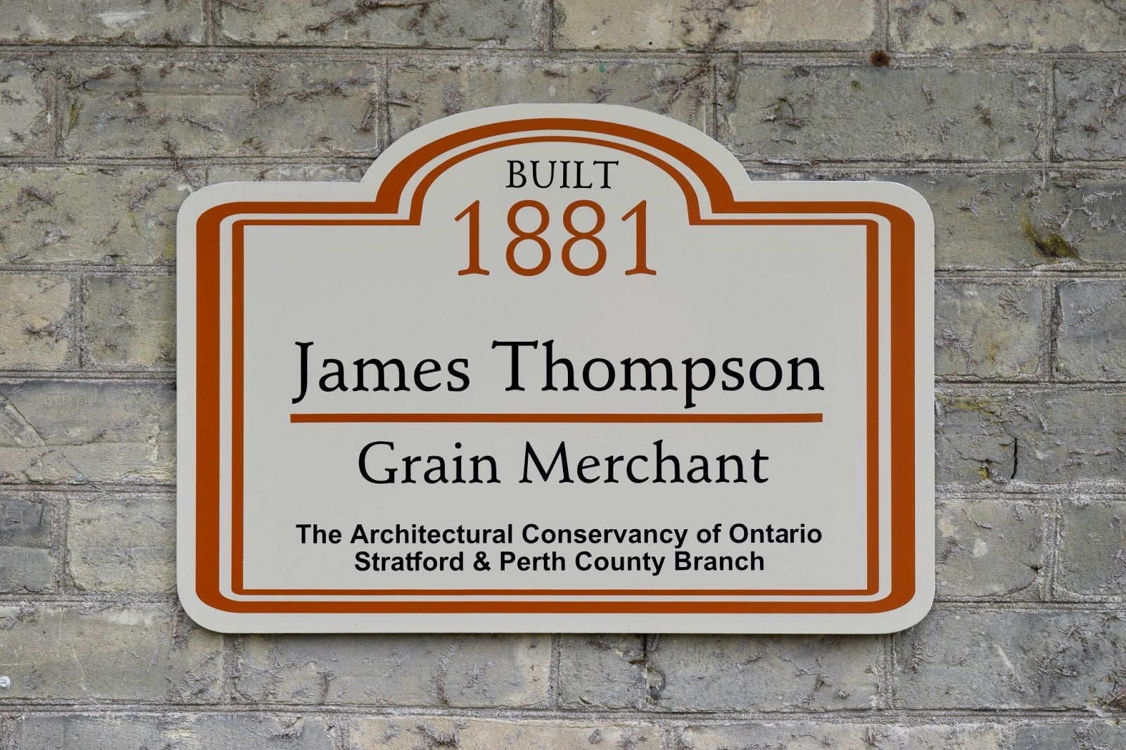 A heritage plaque on a building wall reading "Built 1881, James Thompson, Grain Merchant" 