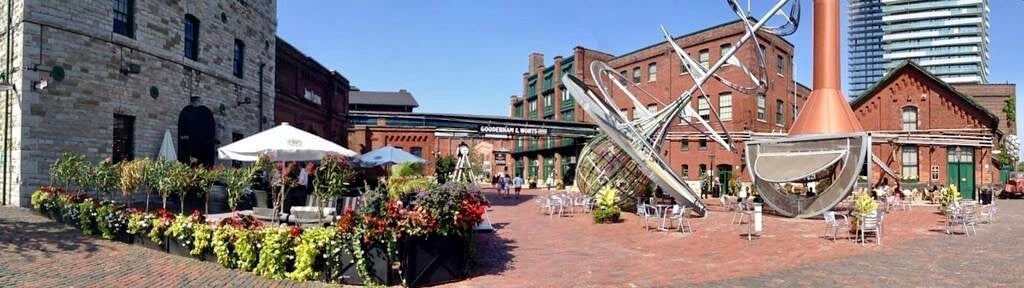 A panoramic view of the centre of the Distillery District in Toronto with historic buildings, restaurant patio, and public art