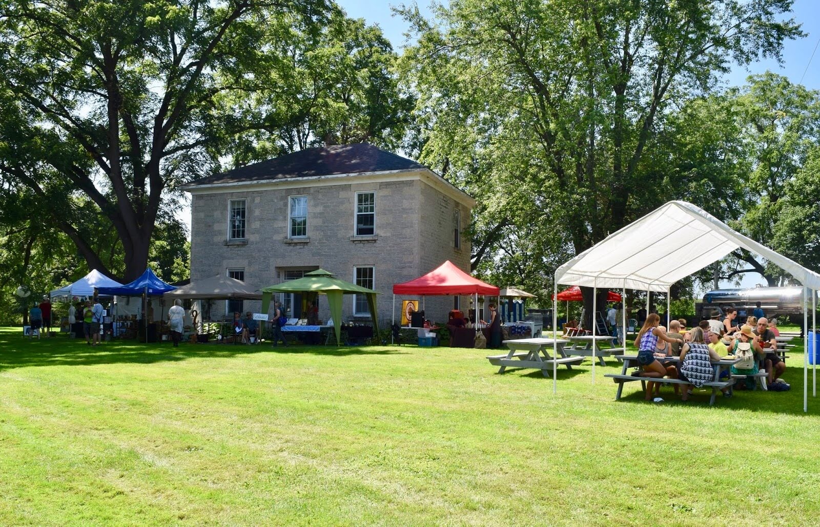 A stone farmhouse during the day with an event going on; people sitting under tents and eating