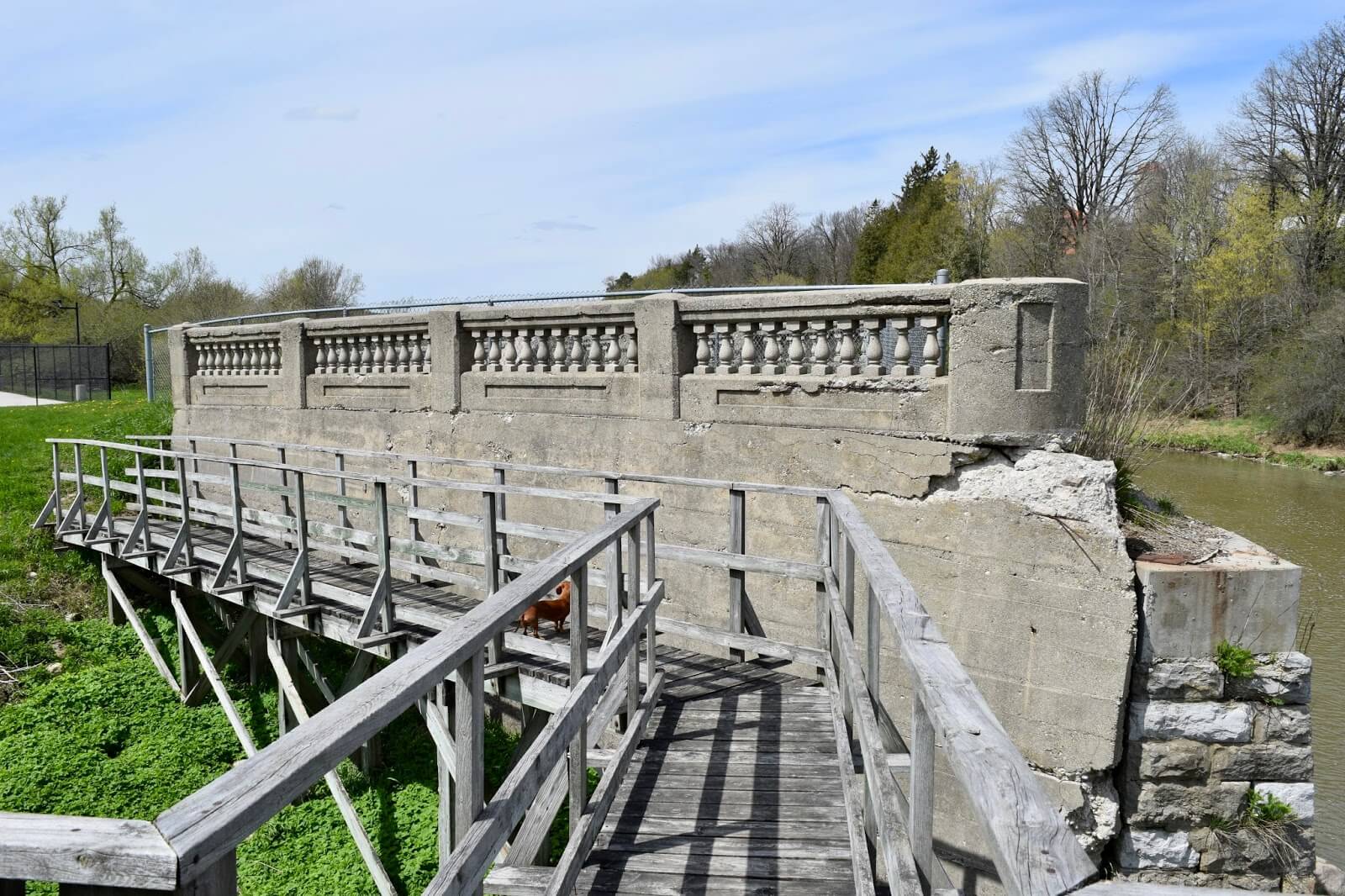 Stone abutments and cement walls of a bridge approach with a wooden walkway in Elmira, Ontario