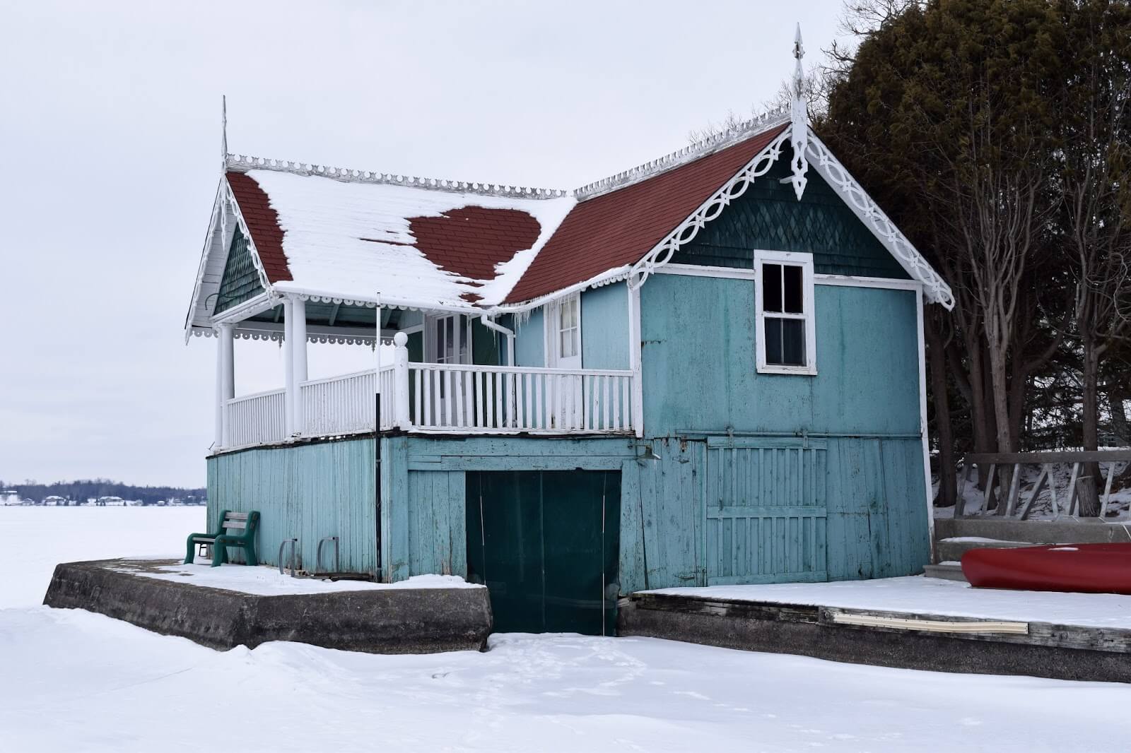 A two-storey boat wooden boathouse with decorative roof finishes painted blue with red shingles and white trim in the winter