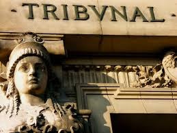 A stone statue of a woman in front of a stone building with the word "tribunal" in-scripted on it