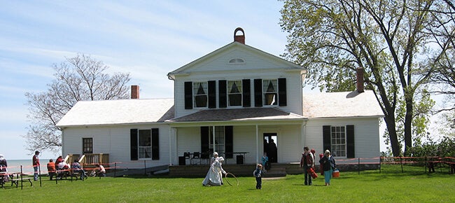 A white house dating back to 1842 with people playing in the front yard at John R. Park Homestead near Kingsville