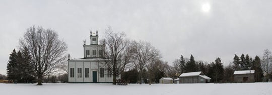 An image of The Sharon Temple in Sharon, Ontario. A temple-style building with tiered storeys and barns surrounding in the winter time