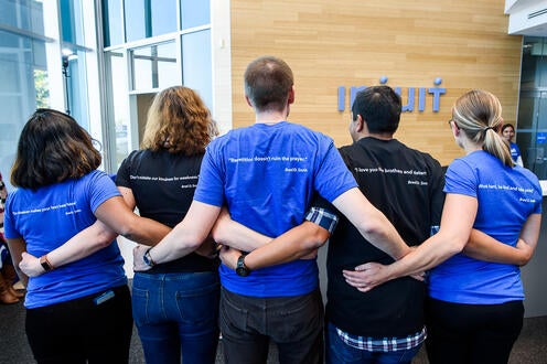 Five Intuit team members standing side by side crossing arms showing off the qutoes on the back of their Intuit t-shirts.