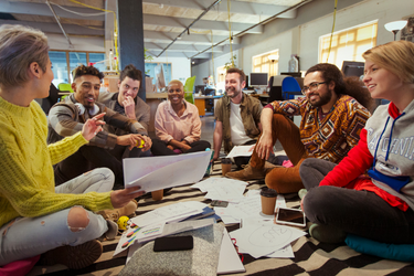 Diverse group of employees at a non-profit sitting in a group smiling, while looking at a project