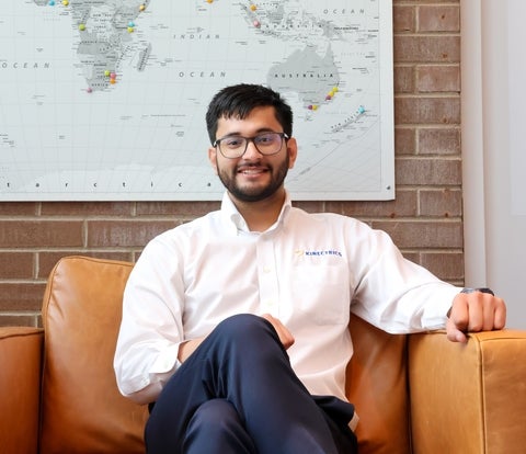 Waterloo alum, Aryan Sharma in a photo pose sitting cross-legged in a brown chair