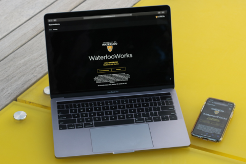 Laptop and phone on a yellow desk with the WaterlooWorks home page open on both devices