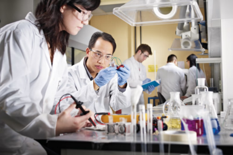 A student stares at circuitry while surrounded by beakers of chemicals in a lab