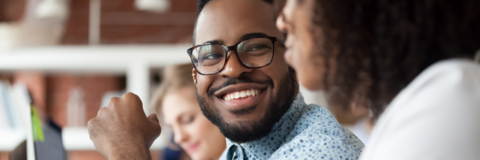 Guy wearing glasses smiling at a co-worker mid conversation