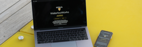 Laptop and phone on a yellow desk with the WaterlooWorks home page open on both devices