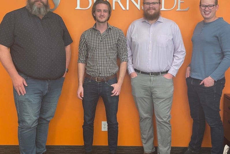 Four R.J. Burnside employees standing in front of the sign at the office