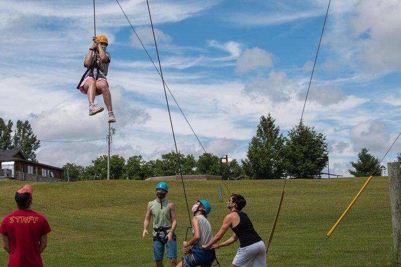 Staff help bring camper down from climbing wall at Camp Brebeuf