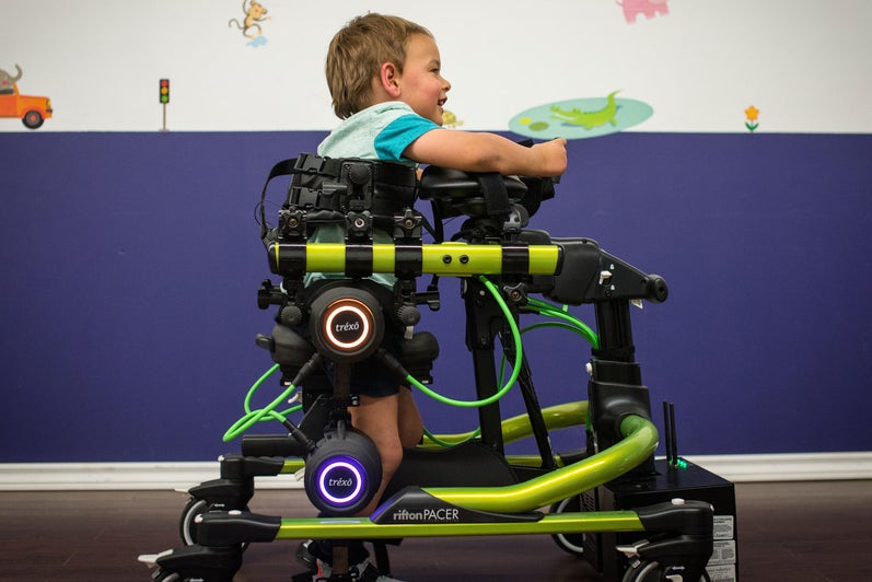 A side view of Noah using the Trexo to walk.
