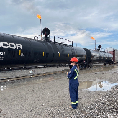 A female co-op student wearing a hard hat infront of a railcar during air monitoring.