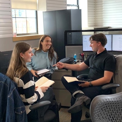 Students sit with a supervisor in an informal meeting setting.
